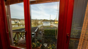 Blick aus einem Fenster mit rotem Rahmen auf einen Garten mit Topfpflanzen und eine Holzterrasse.