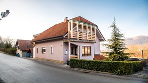 Ein zweistöckiges Haus mit rotem Ziegeldach, einem Balkon und einer kleinen Veranda.