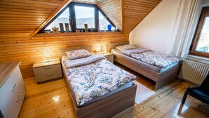 Ein gemütliches Schlafzimmer im Dachgeschoss mit zwei Betten, Holzwänden, einem Dachfenster und Blick ins Freie.