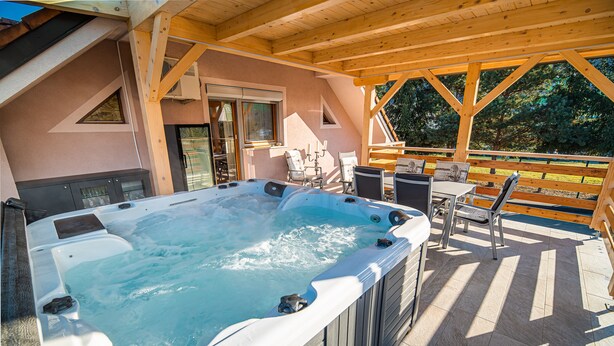 Ein Whirlpool in einem überdachten Außenbereich mit Holzbalken und Blick auf Bäume.