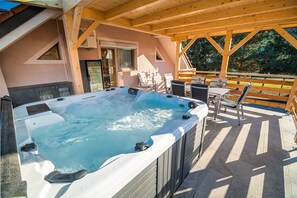 A hot tub in a covered outdoor area with wooden beams and a view of trees.