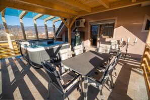 Une terrasse extérieure avec un jacuzzi, une table, des chaises et une vue sur les montagnes.