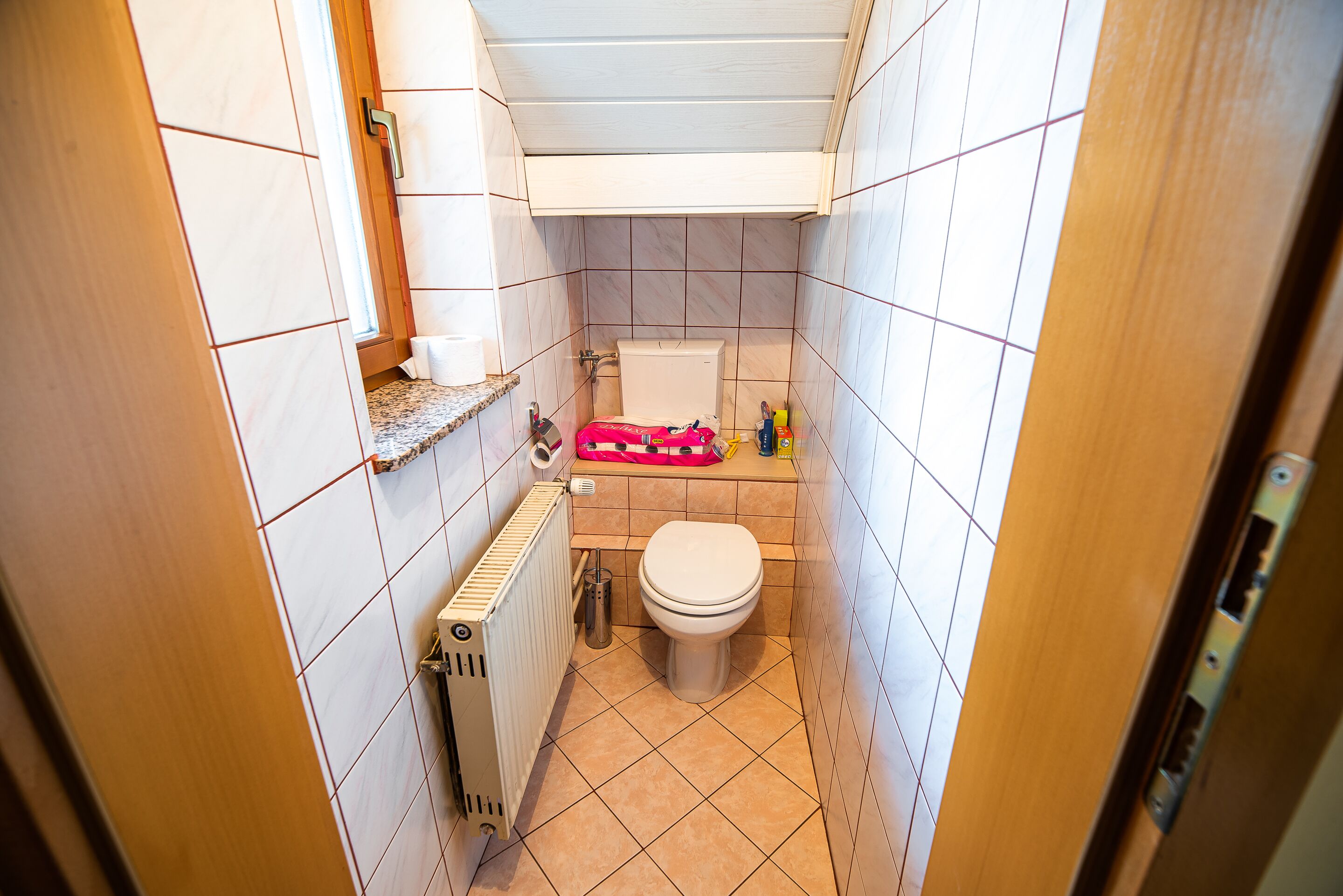 A small bathroom with a toilet, a radiator, and a shelf with toiletries.