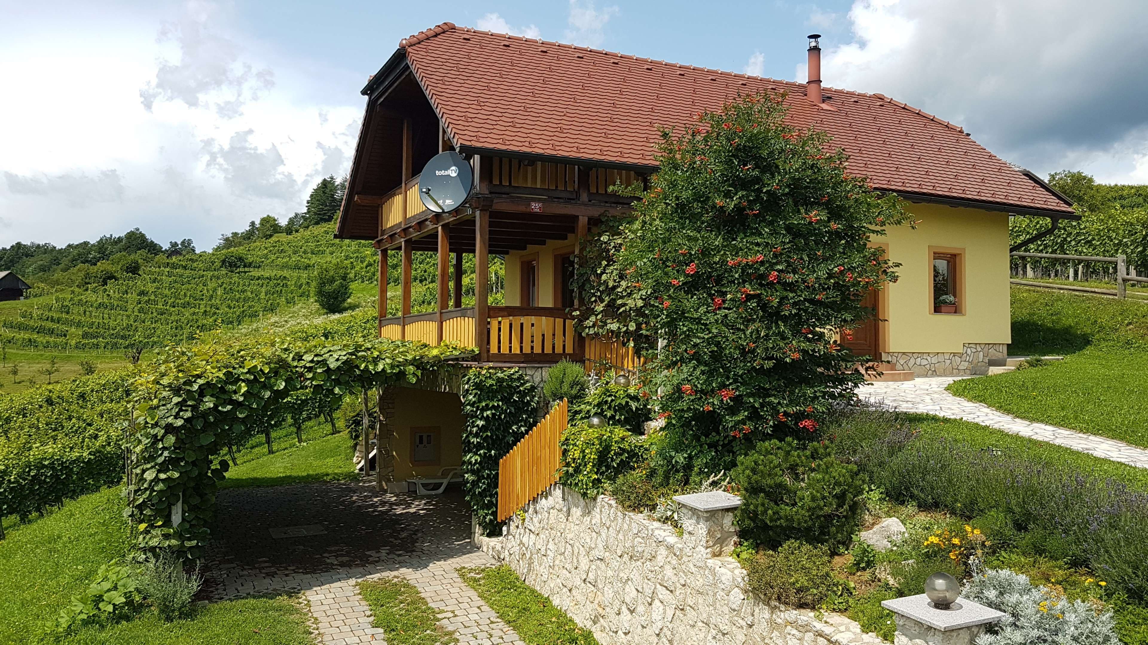 Ein zweistöckiges Haus mit rotem Ziegeldach, einem hölzernen Balkon und einer Satellitenschüssel.