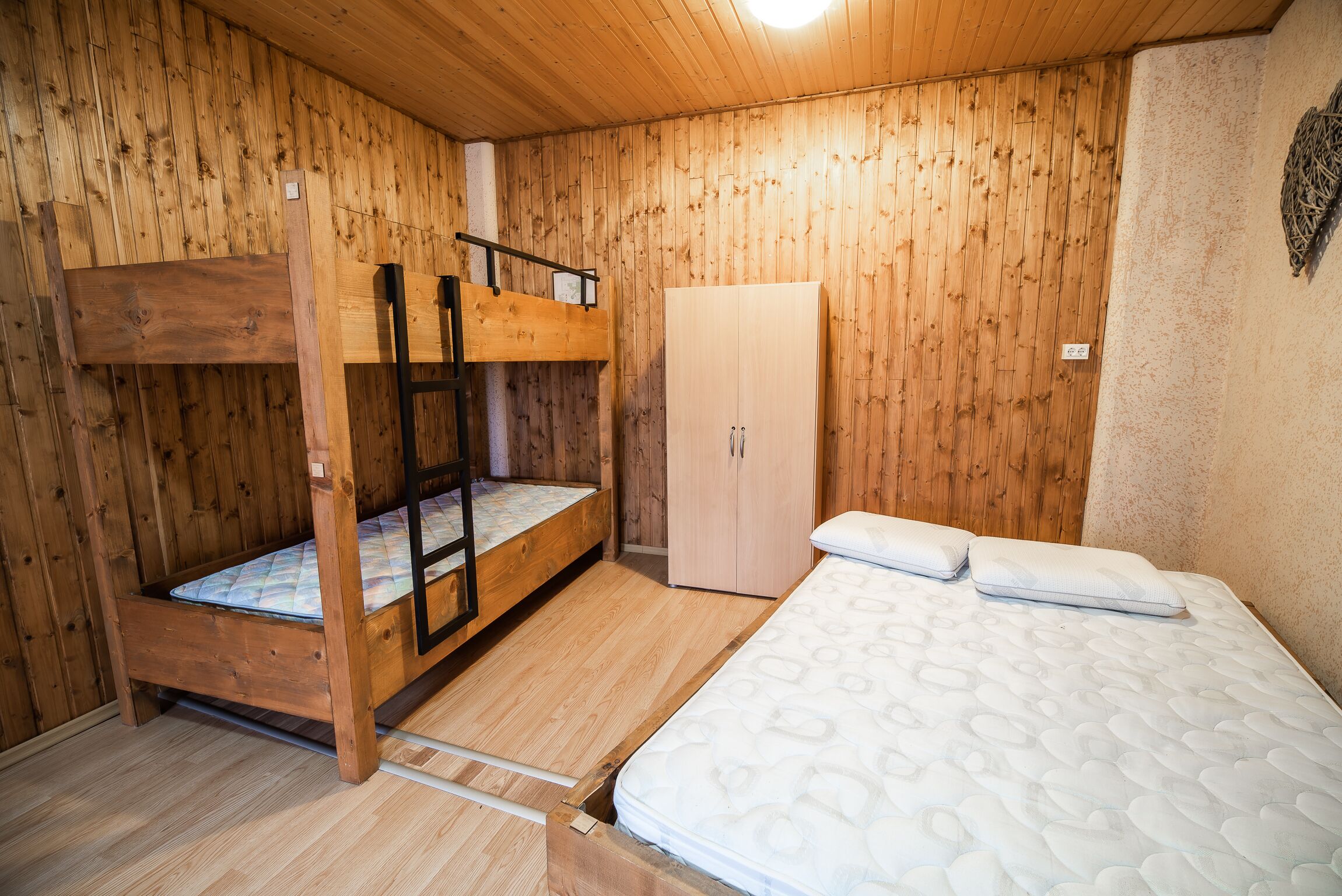 A wooden room with bunk beds, a wardrobe, and a bed with pillows.