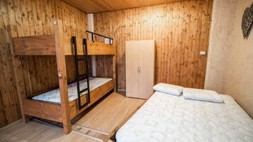 A wooden room with bunk beds, a wardrobe, and a bed with pillows.