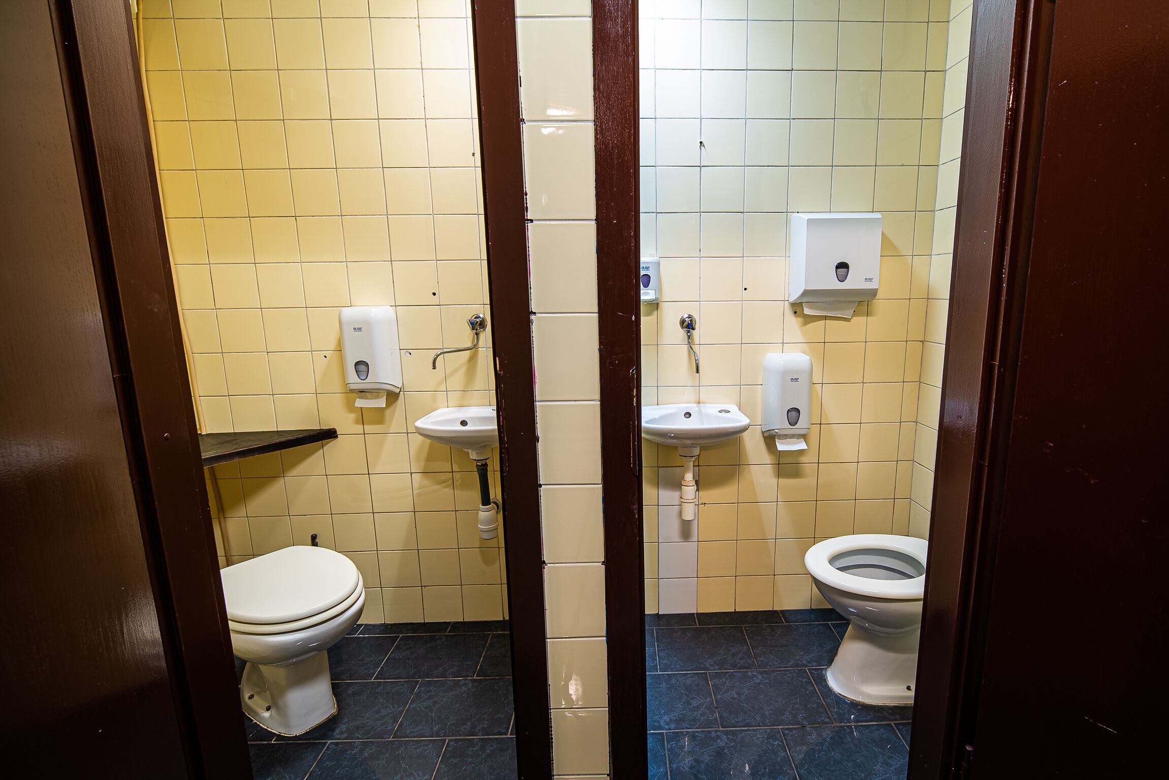Ein kleines Badezimmer mit Fliesen, zwei Toiletten, zwei Waschbecken und Handtrocknern.