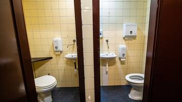 Ein kleines Badezimmer mit Fliesen, zwei Toiletten, zwei Waschbecken und Handtrocknern.
