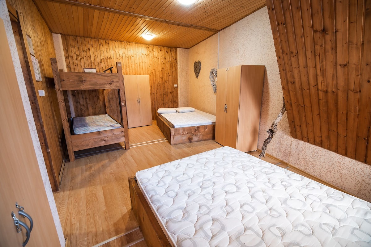 A room with wooden walls and floors, a bunk bed, a single bed, and a wardrobe.