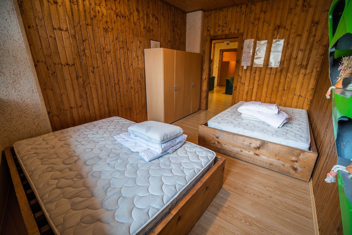 A wooden room with two beds, each with a mattress and pillows, and a wooden wardrobe.