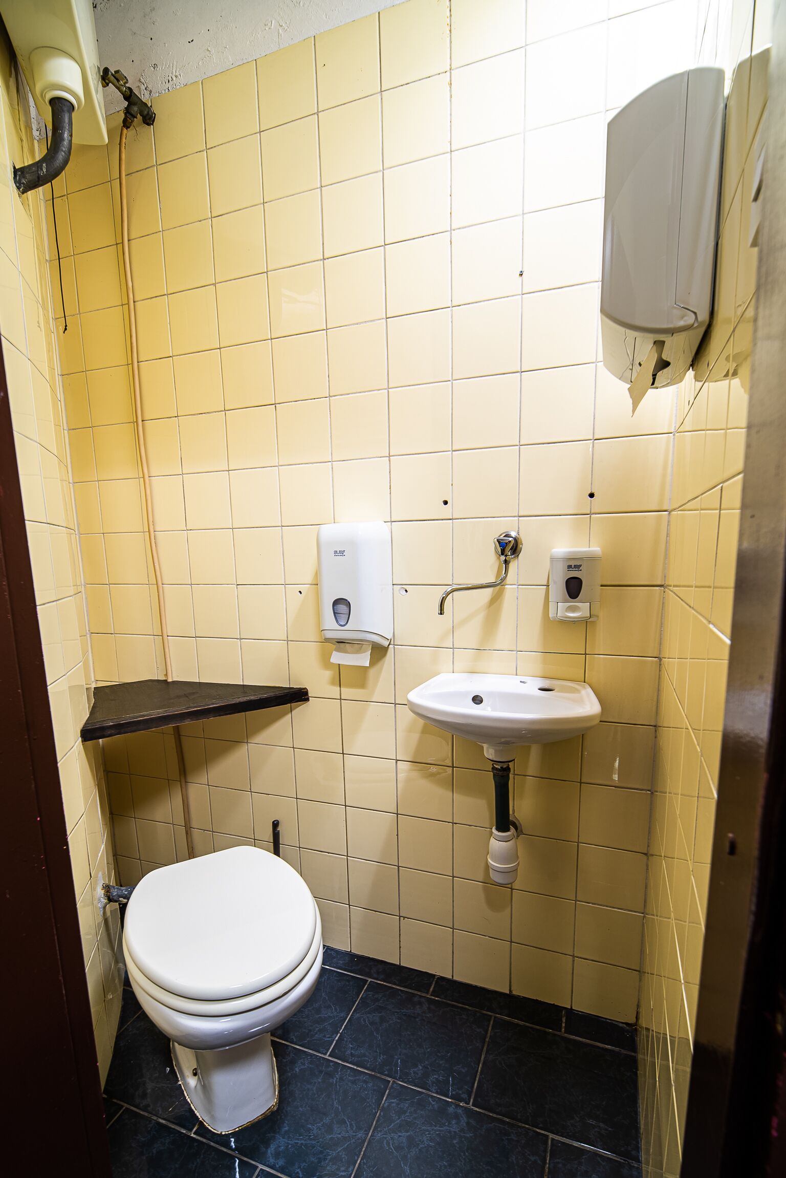 Un baño pequeño con azulejos amarillos, un inodoro blanco, un lavabo negro y un dispensador de jabón.
