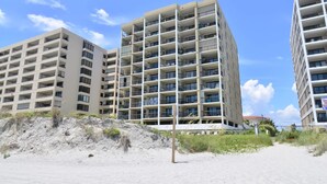 A beachfront hotel with multiple floors, balconies, and a sandy beach area. - Direct Oceanfront Magic at Sea Marsh w Pool (North Myrtle Beach)