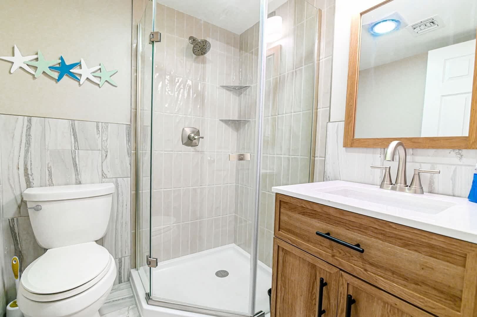 A bathroom with a toilet, shower, and vanity with a mirror.