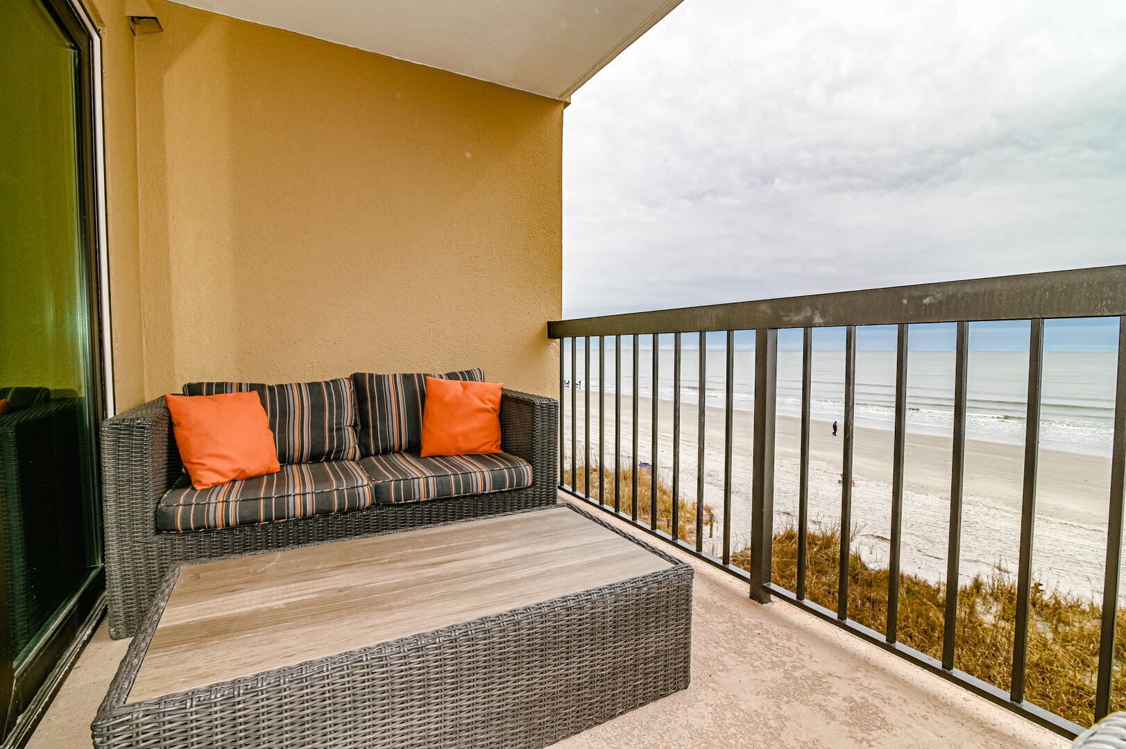 Un balcon avec un canapé et des coussins en osier, donnant sur une plage.