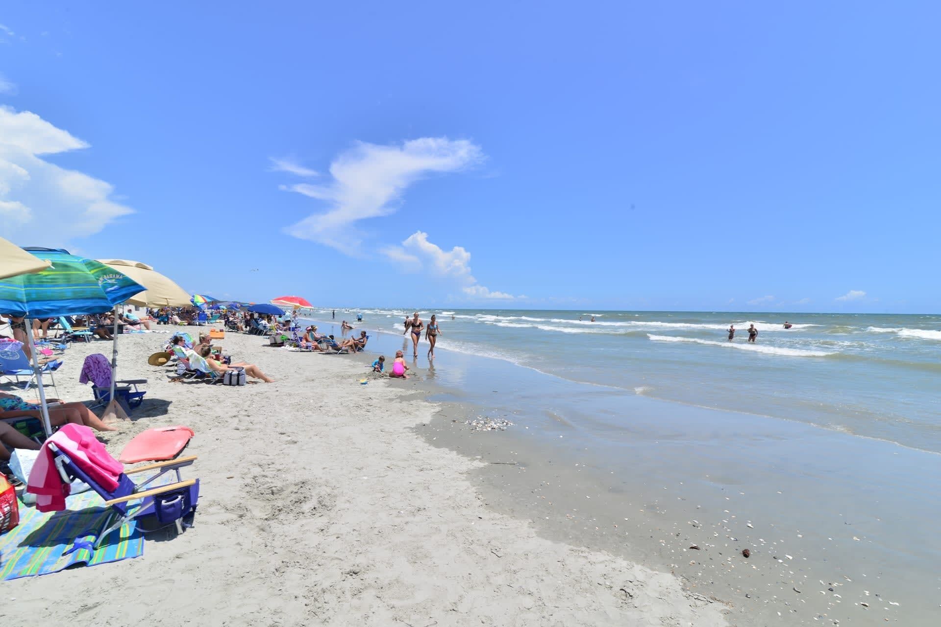 A beach with umbrellas, beach chairs, and people.