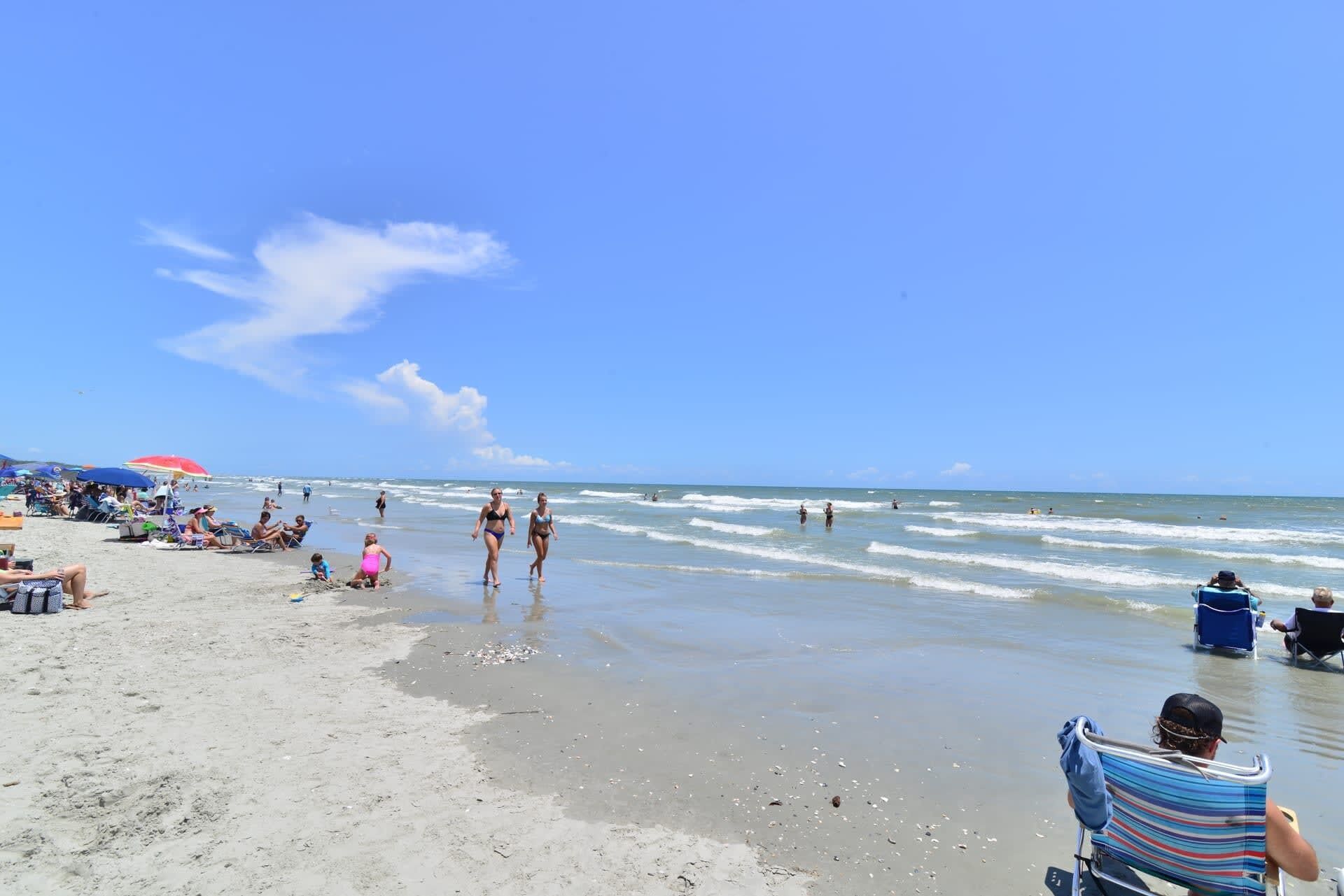 A beach with people walking and sitting, umbrellas, and a clear sky.