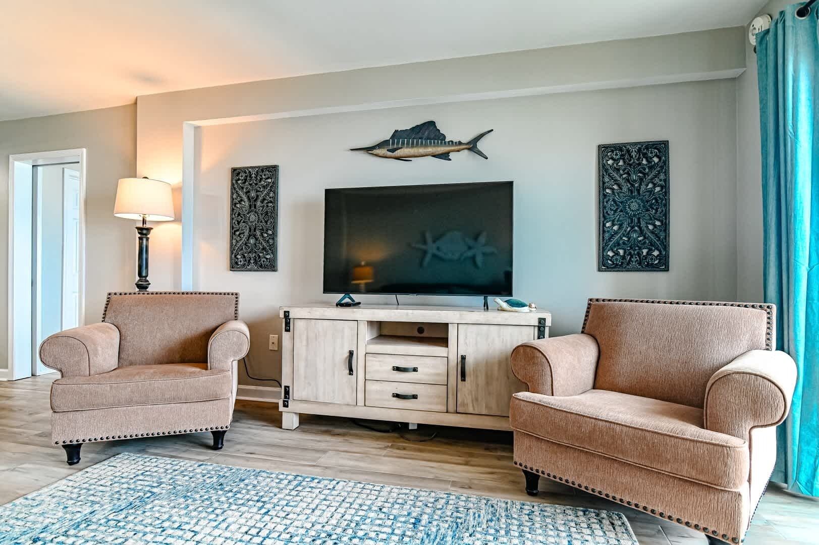 A living room with two armchairs, a TV, a cabinet, and decorative wall art.