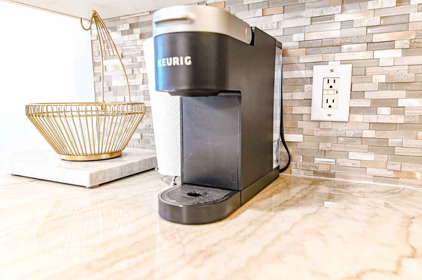 Une machine à café Keurig posée sur un comptoir de cuisine, avec un mur recouvert de carreaux et une prise électrique à proximité.