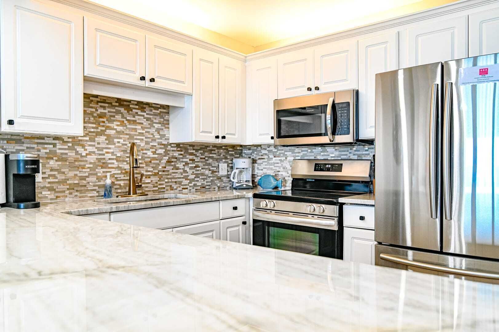 A modern kitchen with white cabinets, a stainless steel refrigerator, a microwave, a coffee maker, and a tiled backsplash.