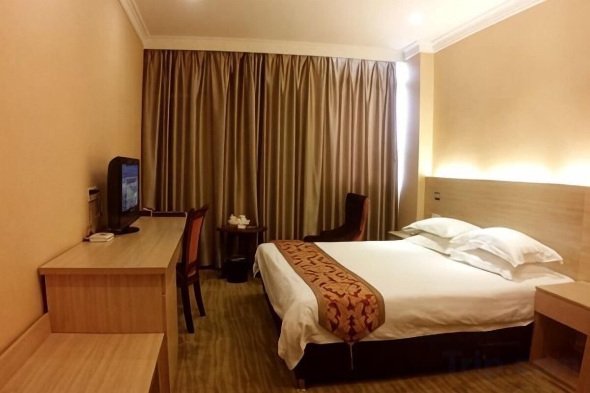 A hotel room with a bed, a desk, a chair, a television, and a curtain.