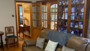 A living room with a leather sofa, a wooden chair, and a glass cabinet filled with decorative items. - Remarkable 2-bed Cottage in Tranquil Setting (Wooler)