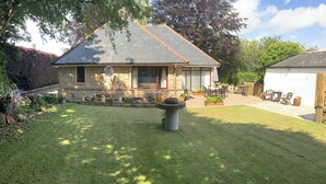 A stone house with a sloped roof, a well-maintained lawn, and outdoor furniture. - Remarkable 2-bed Cottage in Tranquil Setting (Wooler)