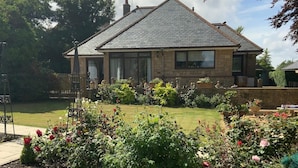 A two-story house with a pitched roof, stone exterior, and a well-maintained garden with various plants and flowers. - Remarkable 2-bed Cottage in Tranquil Setting (Wooler)