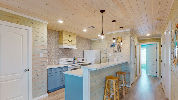 Une cuisine avec des meubles en bois, un îlot central doté de tabourets et des luminaires suspendus.