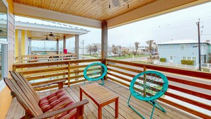 Une terrasse extérieure couverte, dotée de bancs et de chaises en bois, d’une table et offrant une vue sur le quartier environnant.