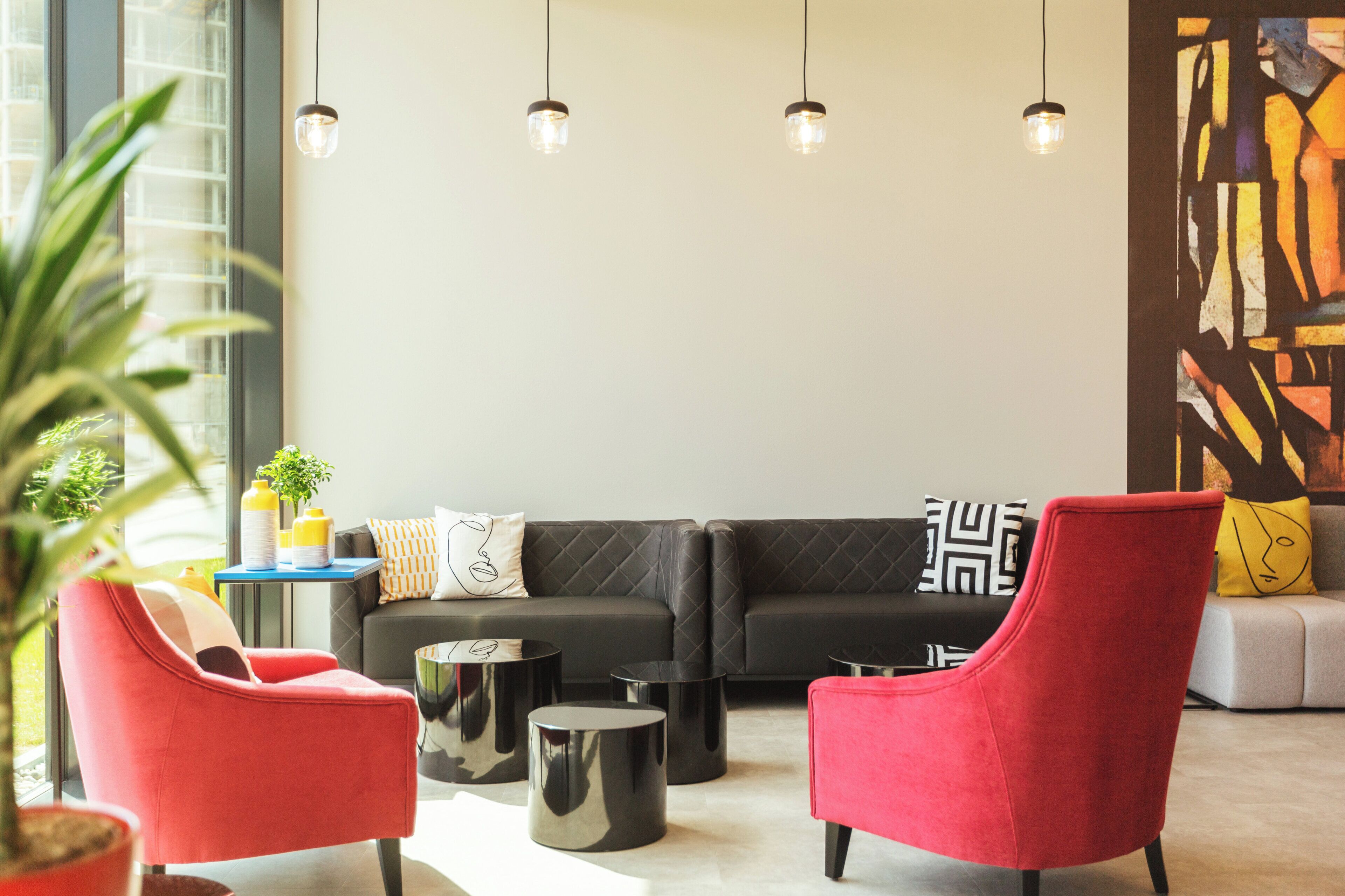 A modern living room with a black sectional sofa, red armchairs, and a round coffee table.