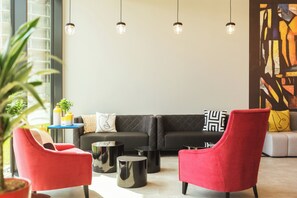 A modern living room with a black sectional sofa, red armchairs, and a round coffee table. - Holiday Inn - the niu, Form Stuttgart Feuerbach by IHG (Stuttgart)