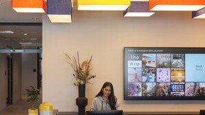 A reception desk with a digital display above it, a potted plant, and a yellow vase.