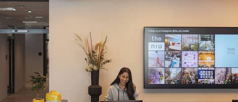 A reception desk with a digital display above it, a potted plant, and a yellow vase.