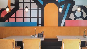 A restaurant with a modern interior, featuring a colorful abstract mural, wooden booth seating, and pendant lighting. - Holiday Inn - the niu, Form Stuttgart Feuerbach by IHG (Stuttgart)