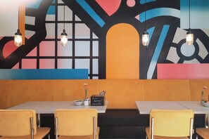 A restaurant with a modern interior, featuring a colorful abstract mural, wooden booth seating, and pendant lighting. - Holiday Inn - the niu, Form Stuttgart Feuerbach by IHG (Stuttgart)