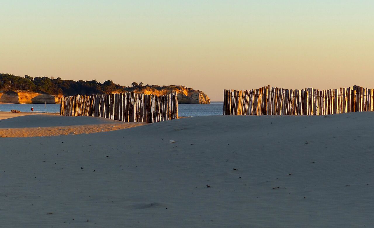 Une plage avec des structures en bois, un rivage sablonneux et une falaise rocheuse en arrière-plan.