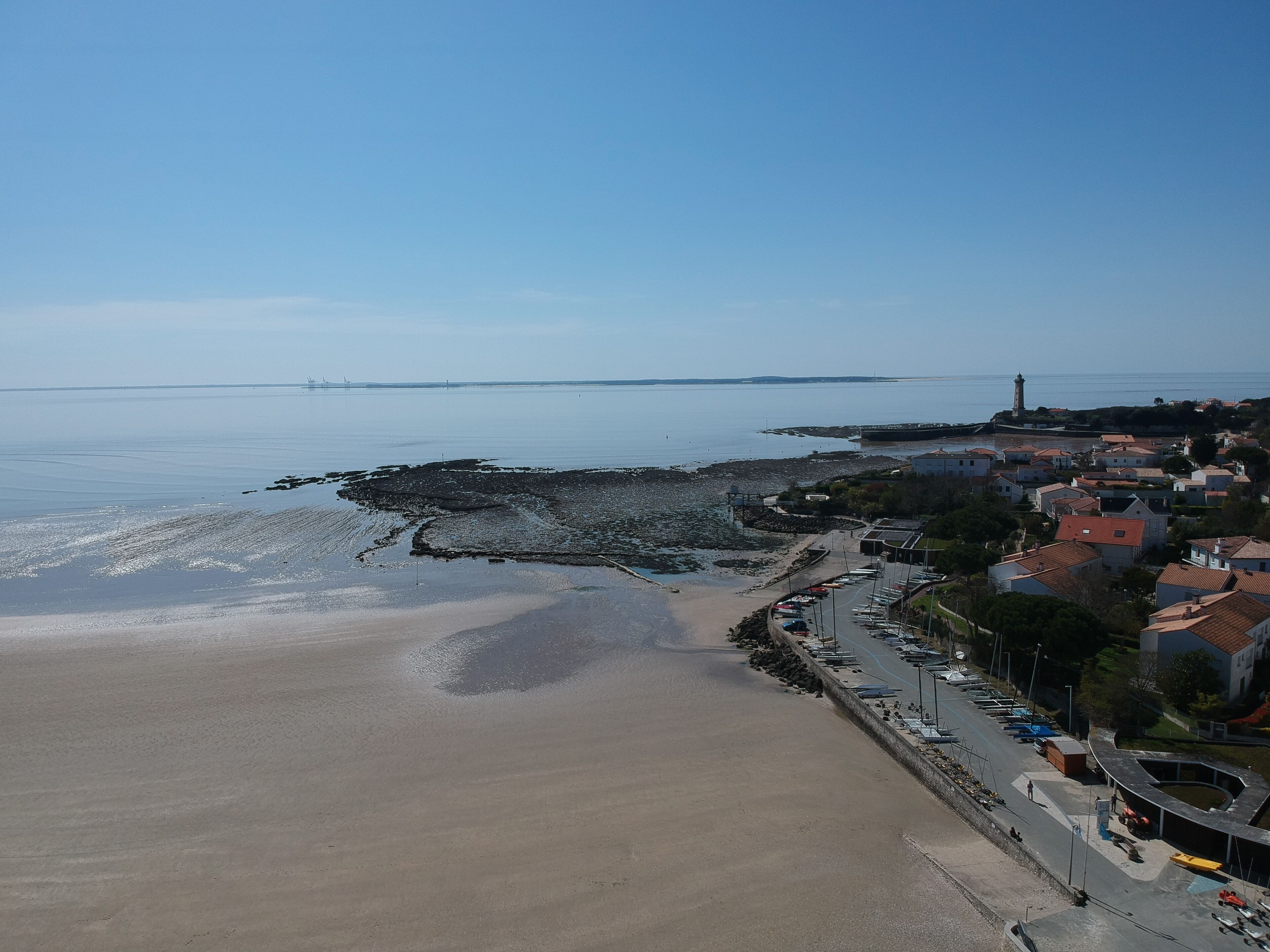 A coastal town with a sandy beach, a lighthouse, and a row of houses with red roofs.
