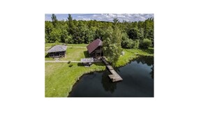 En træhytte med rødt tag og en anløbsbro, der strækker sig ud i en sø, omgivet af tæt skov.