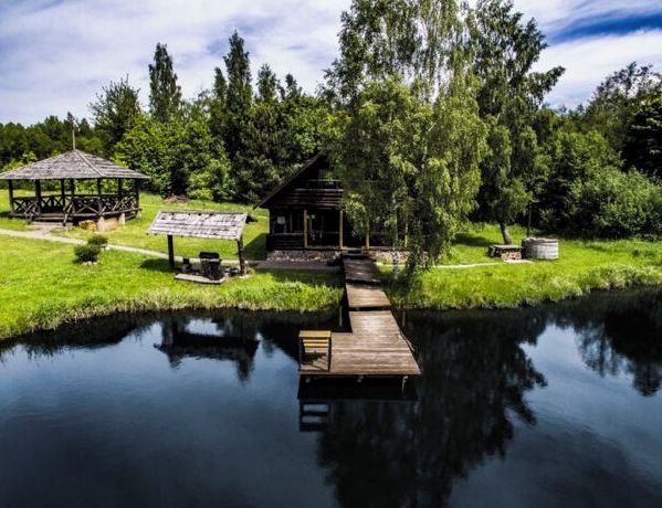 Ein rustikales Holzhäuschen an einem stillen See mit einer Holzsteg, der darauf führt, umgeben von üppiger Vegetation und Bäumen.