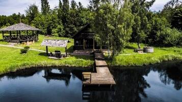 Ein rustikales Holzhäuschen an einem stillen See mit einer Holzsteg, der darauf führt, umgeben von üppiger Vegetation und Bäumen.