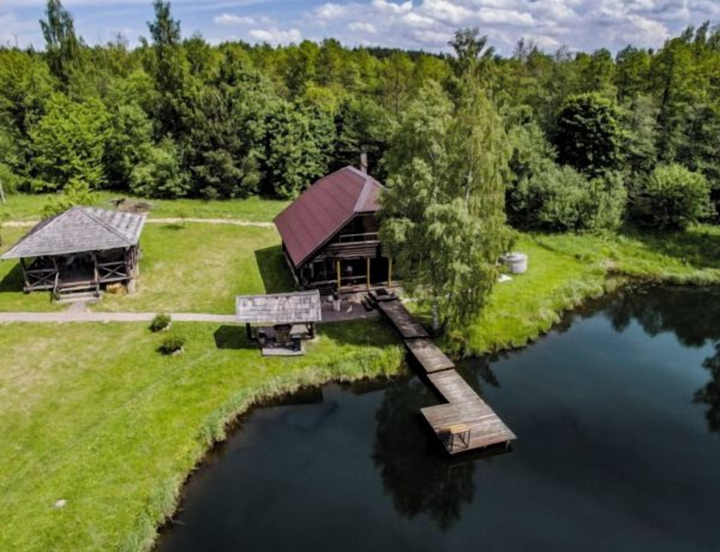 Eine Holzhütte mit rotem Dach und einem Steg, der in einen See hineinreicht, umgeben von dichtem Wald.