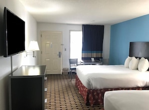 A hotel room with a bed, a desk, a TV, a chair, and a window with curtains.