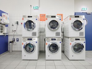 Une rangée de machines à laver à chargement frontal, toutes blanches et superposées, dans une laverie industrielle.