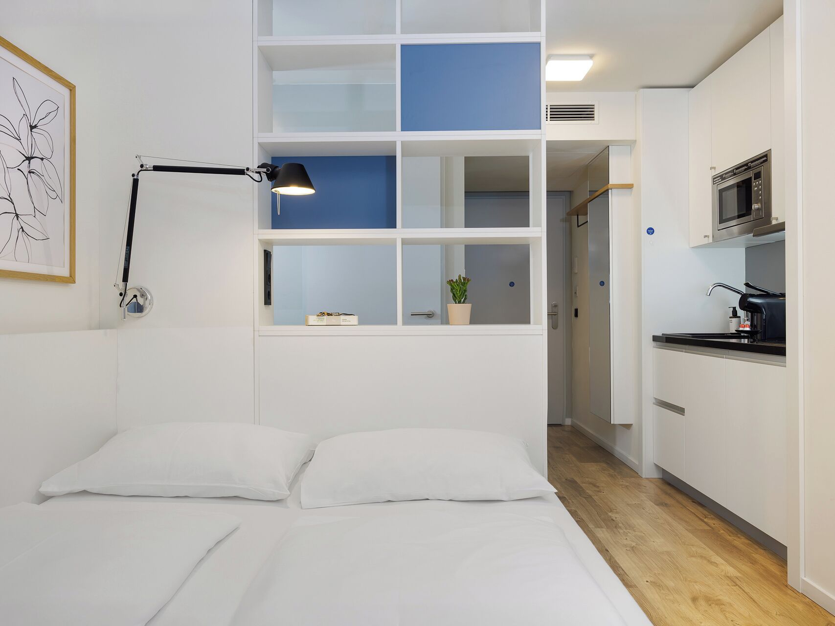 Een moderne slaapkamer met een bed, bedlamp en uitzicht op een keuken met een magnetron.