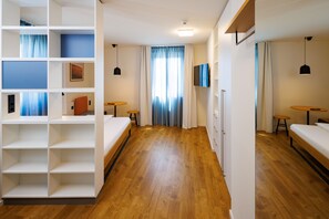 Une chambre d’hôtel avec un plancher en bois, un lit, un bureau, une chaise, une armoire et un téléviseur fixé au mur.