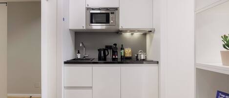 A compact kitchen with white cabinetry, a microwave, a coffee maker, and a potted plant.