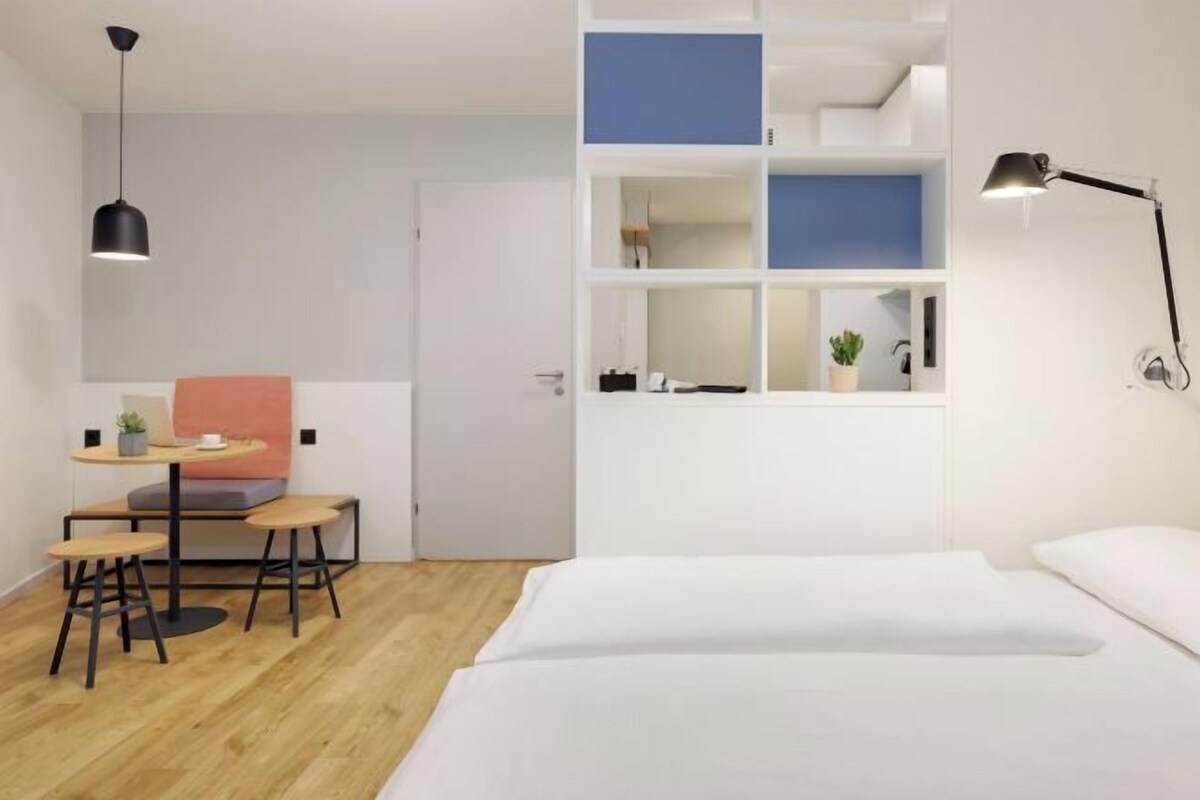 Quarto com cama, escrivaninha com cadeira, luminária pendente e prateleira com objetos.