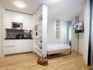 A compact room with a kitchenette, a bed, a TV, and a bag on the floor. - smartments Wien Heiligenstadt (Vienna)