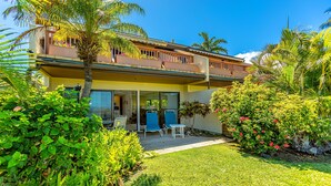 A two-story building with a balcony, a lawn, and tropical plants.