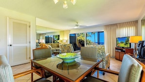 A hotel room with a dining area, a television, and a view of the ocean.